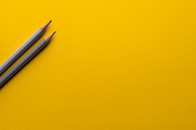 Two grey pencils on a yellow backdrop