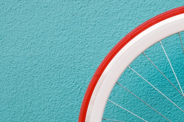 A red tire on a white-rim bike wheel that detaches from the textured turquoise wall behind it